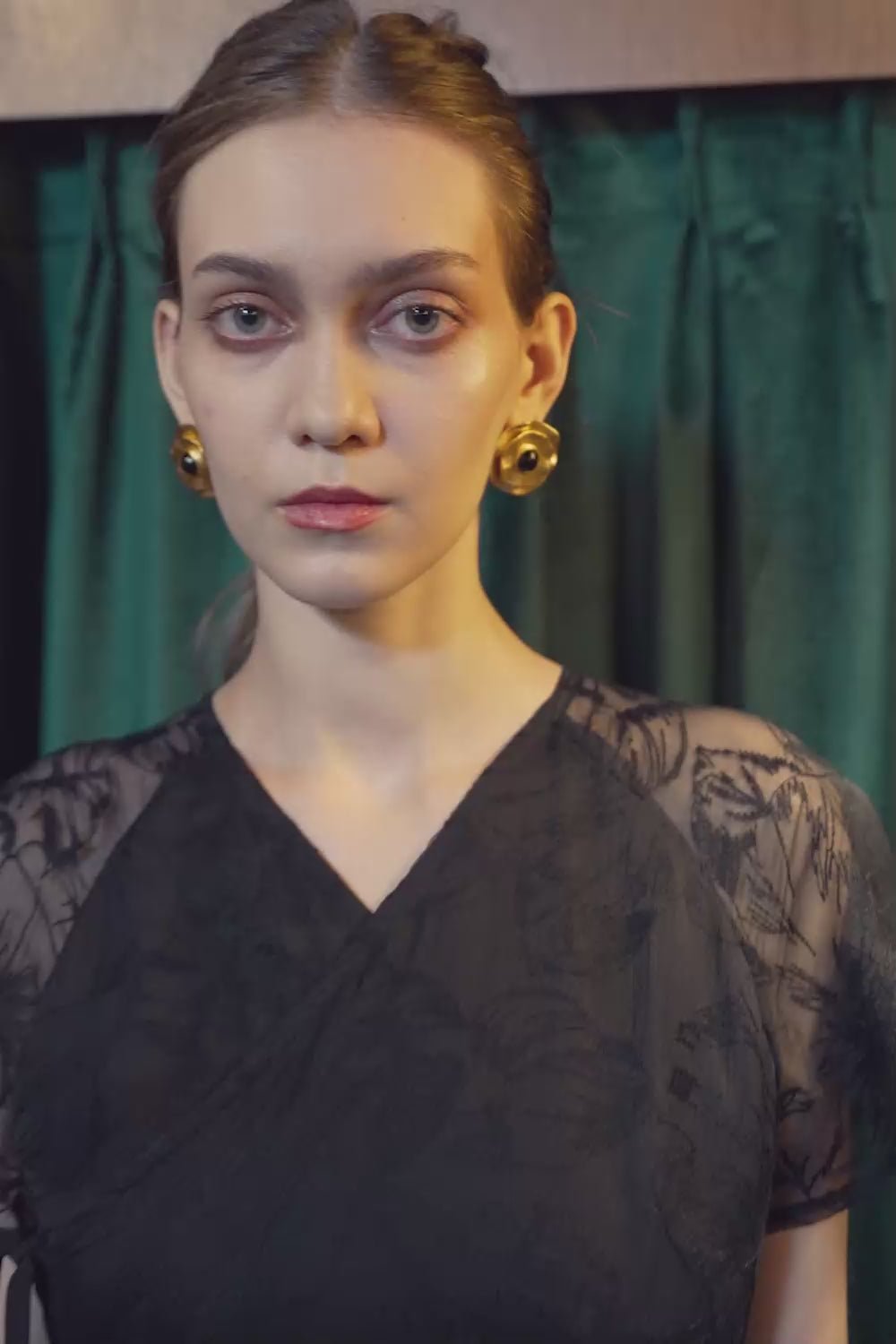 Model walking in the BEHOLD Flutter Sleeves Wrap Midi Dress in black lace, featuring V-neckline, sheer flutter sleeves, and wrap silhouette, showcasing fluid movement indoors against a green curtain backdrop.