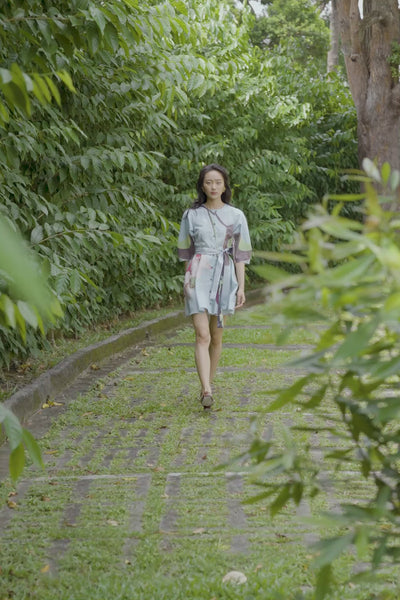 Woman walking in ABIDE placement print mini dress with contrast sash belt in outdoor garden setting