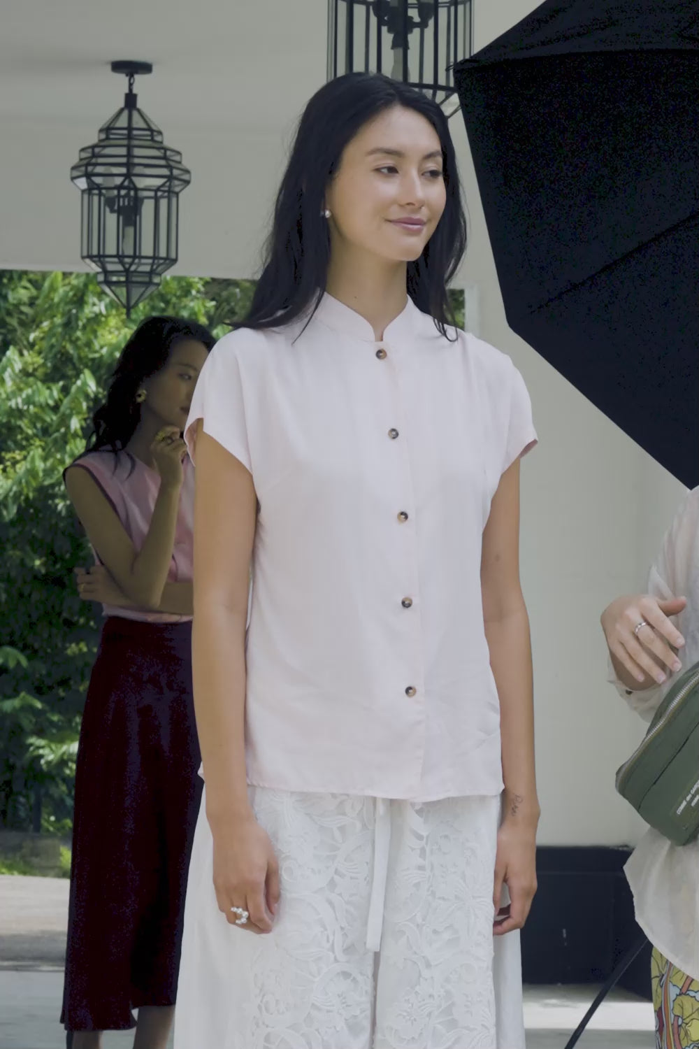 Close-up video of woman wearing soft pink micro Chinese collar blouse with button front, paired with white lace wide-leg pants