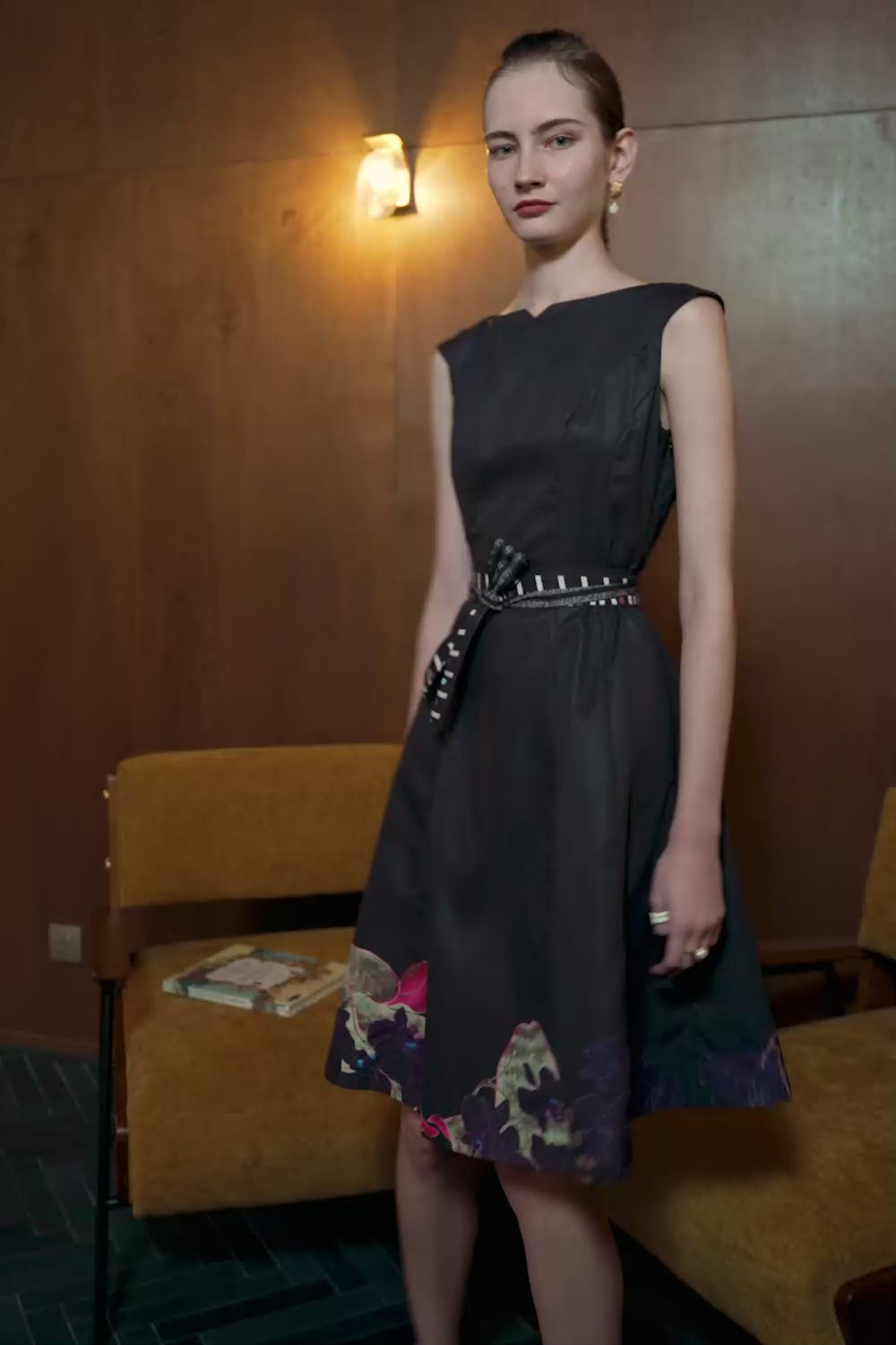 Model in black bateau cap sleeve dress with Dendrobium Orchid print at hem — structured fit with belted waist