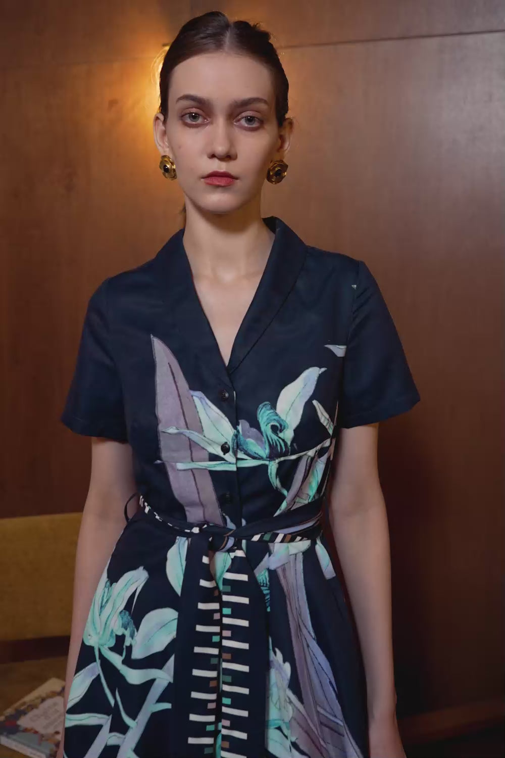 Model in Cymbidium Orchid panel dress with shawl collar — navy silhouette with floral print and striped waist sash