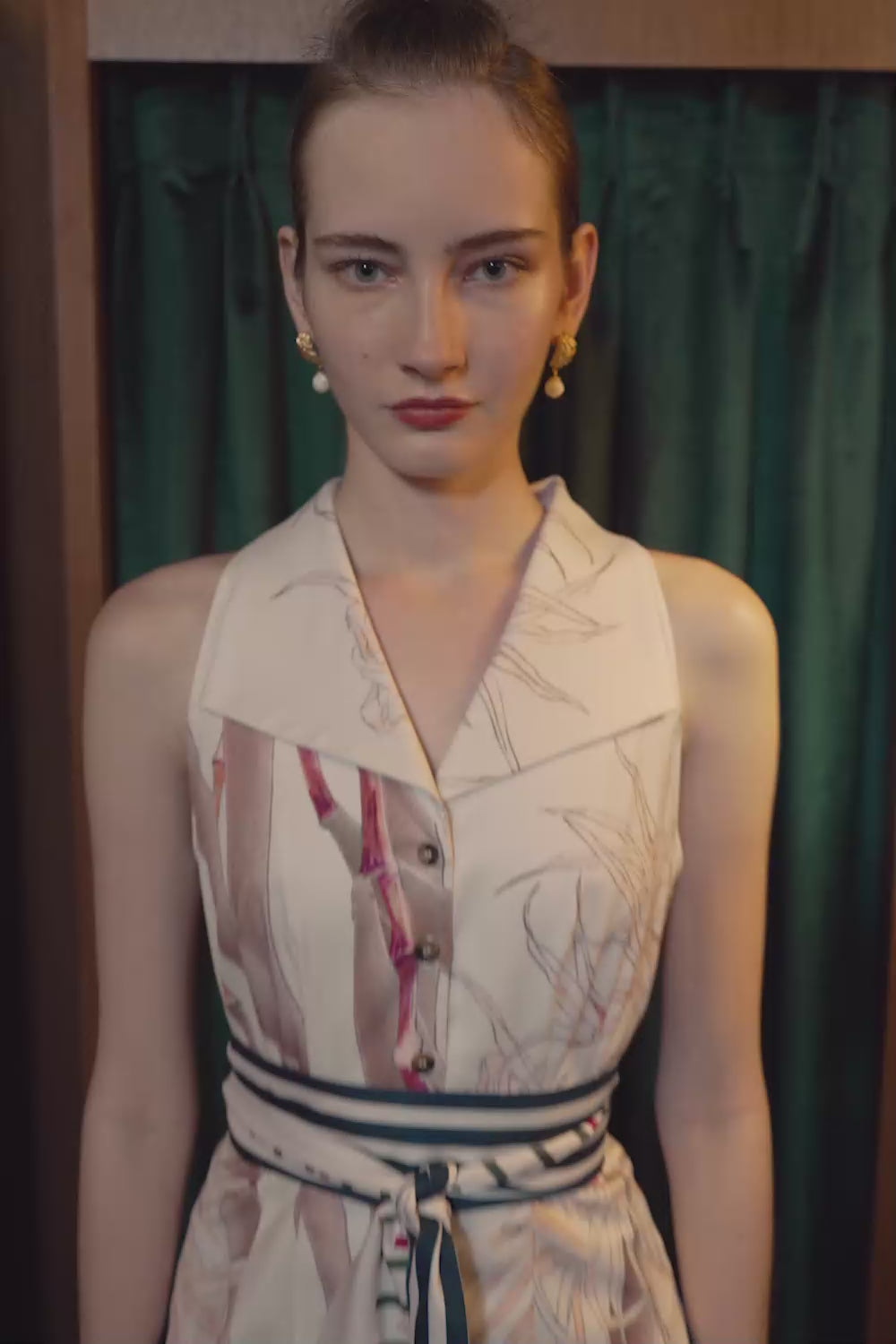 Video of a model wearing the Pilgrim Racer Vest and Godet Skirt in navy and red, standing in front of deep green curtains framed by wood panels and warm lighting.